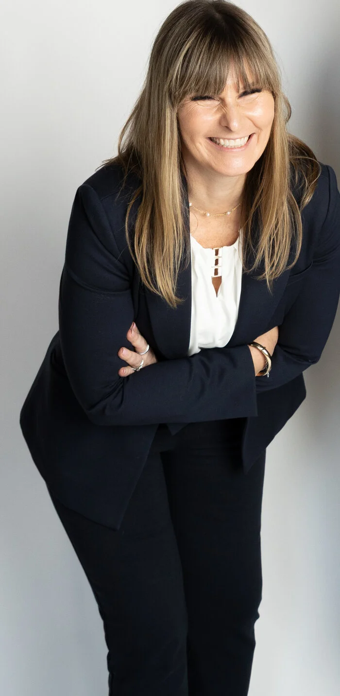 Maria laughing and leaning forward in a navy suit